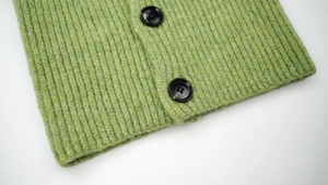 Close-up of green rib-knit wool scarf detail with two textured dark round buttons