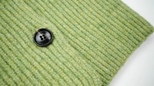 Detail shot of bright green knit wool scarf featuring ribbed texture and black button