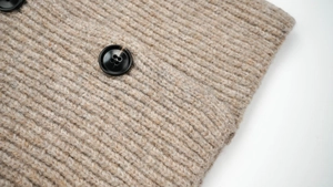 Close-up of oatmeal wool knit texture with a black round four-hole button detail