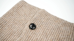 Close-up of beige ribbed knit texture and black button detail on winter wool snarf