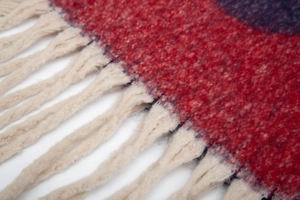 Gros plan détaillé des glands beiges sur une écharpe en jacquard géométrique rouge et bleu