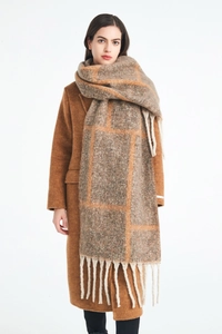 Detail of soft thick knit scarf featuring brown plaid pattern and white fringe tassels