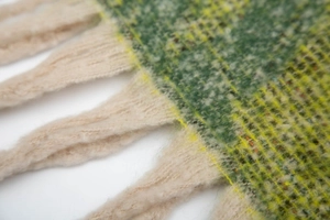 Macro shot of thick winter knit shawl with green plaid pattern and cream tassel fringe