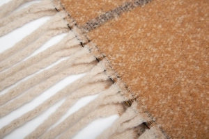 Macro detail of plaid knit scarf with soft mohair texture and long white tassel fringe