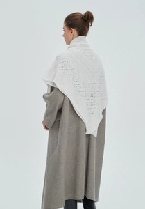 Detail view of a white hollow-out knitted shawl with geometric patterns on a grey coat