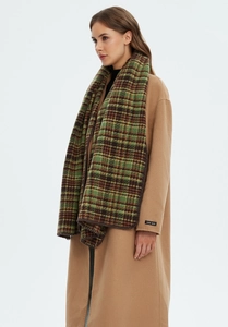 Detail of a green plaid scarf styled with a camel coat featuring a handmade label