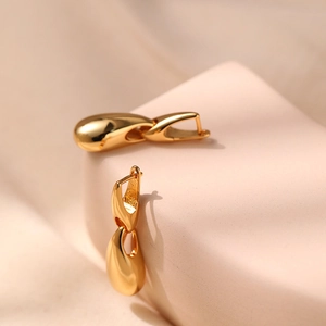 Elegant gold teardrop earrings with a high-polished finish on a minimalist display stand