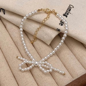 Bracelet de perles blanches élégant avec nœud et chaîne réglable dorée sur socle beige