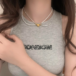 Detail of double-layer necklace with white pearls and gold heart pendant on model