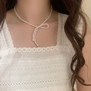 Detailansicht einer weißen Perlen-Schleifen-Halskette mit eleganten Quasten am Model