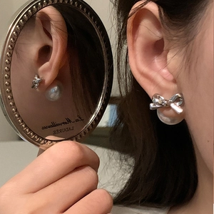 Detailed view of silver bow pearl earrings with mirror reflection on elegant model