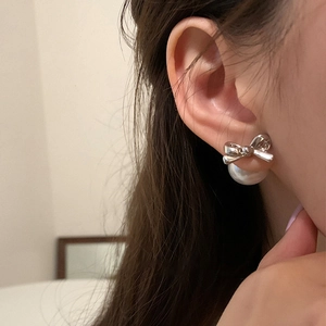 Silver bow stud earrings with large white pearls worn by a model in soft lighting