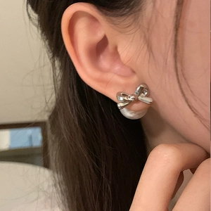 Close-up of elegant silver bow pearl earrings worn on ear with soft lighting