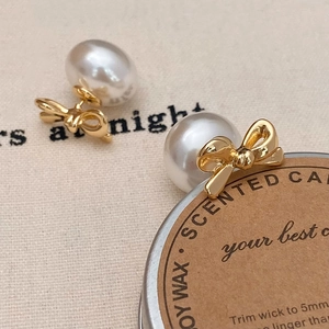 Close-up of elegant silver bow earrings with glossy white pearls on a textured background