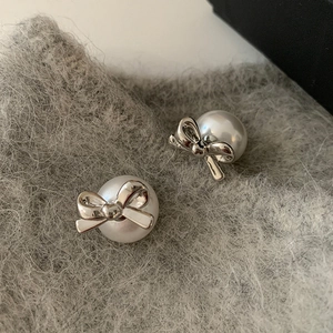Detailed view of silver bow-knot stud earrings with lustrous white pearls on plush fabric