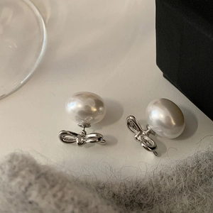Detailed view of silver bow-knot earrings with lustrous white pearls on soft fabric