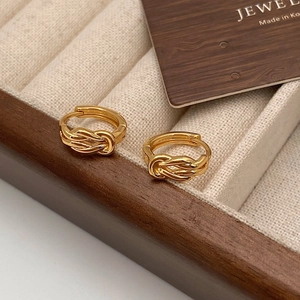 Detail shot of golden lucky knot hoop earrings on a textured jewelry display stand