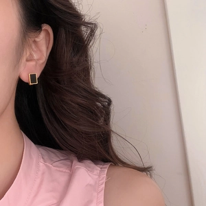 Close-up of minimalist black geometric earrings with gold trim worn by a model