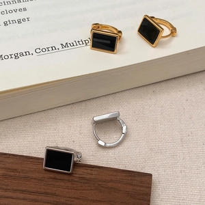Macro shot of geometric gold and silver hoop earrings with rectangular black inlays