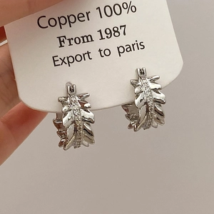 Detail of silver leaf-shaped copper earrings with inlaid sparkling zircon accents