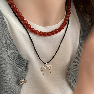 Detail of layered necklace featuring red beads and a silver bow pendant on model