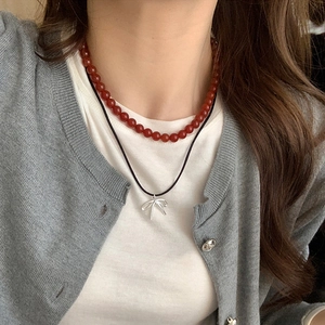 Detail of a double-layered necklace featuring reddish beads and a silver bow pendant