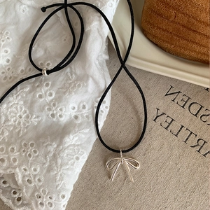 Detail of silver bow pendant on black adjustable cord necklace over lace background