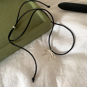Minimalist silver bow pendant necklace on black drawstring over a white fabric background