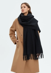 Detailed view of black cashmere-like knit scarf with elegant fringe on a model