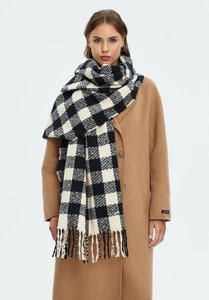 Close-up of black and white checkerboard scarf with long tassel details on a camel coat