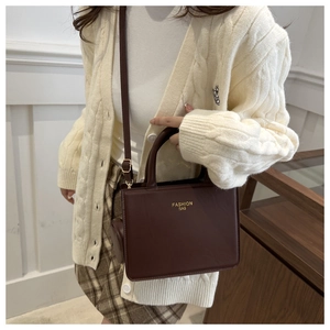 Detail of dark brown leather tote bag with gold lettering shown on a model