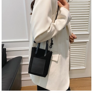 Side view of a minimalist black mini tote bag worn by a model in a white blazer
