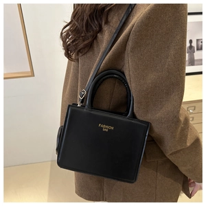 Detail shot of a black PU leather crossbody bag with top handles on a brown suit model