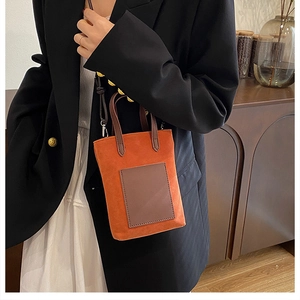 Close-up of mini orange faux suede tote bag with brown leather pocket and crossbody strap