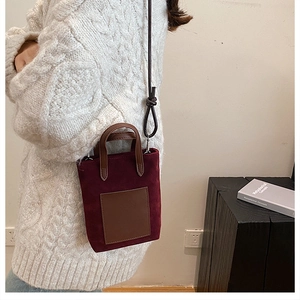 Close-up of a burgundy suede crossbody bag with brown handles on white knit sweater