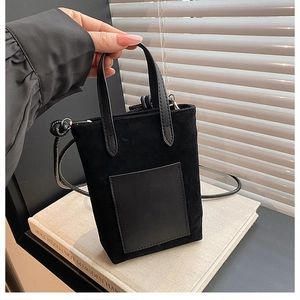 Detail of a minimalist black suede mini tote bag on a white book with natural light