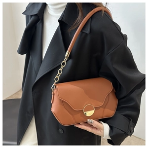 Detail of caramel shoulder bag with wave-edge flap and golden circular metal lock