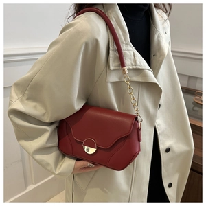 Detail of burgundy leather shoulder bag with gold clasp shown on a beige trench coat
