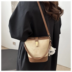 Detail of color-block bucket bag with metal lock and plush charm on shoulder