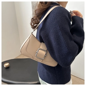 Détail du sac porté épaule beige avec boucle argentée porté sur un pull bleu