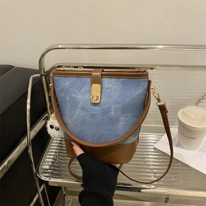 Blue denim and brown leather bucket bag with gold clasp and plush pendant on a shelf