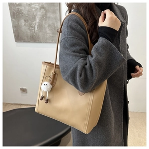 Beige oversized tote bag shown on shoulder with a cute plush charm and minimalist design