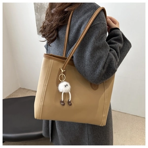 Detail of beige and brown tote bag with plush monster charm worn over shoulder