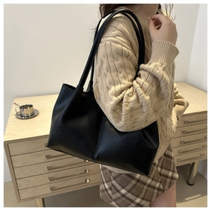 Close-up of black leather tote bag with long straps worn on shoulder by model in knitwear