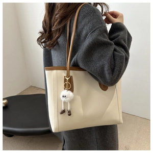 Detail view of the large off-white tote bag with brown leather trim and plush pendant