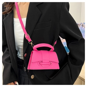Détail du mini sac bandoulière rose en cuir avec boucle dorée sur un blazer noir élégant