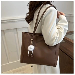 Detail of dark brown matte leather tote bag with a cute white plush monster charm