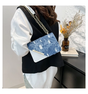 Close-up of denim patchwork shoulder bag with distressed texture and gold chain strap