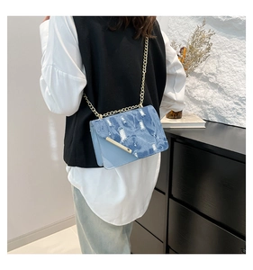 Detail of denim crossbody bag with distressed edges and gold chain strap on model