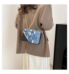 Detail of blue denim and black leather crossbody bag with gold chain strap on a model